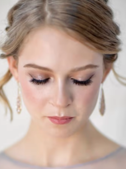 Photo of a woman with an updo, looking down, lashes, and glam makeup