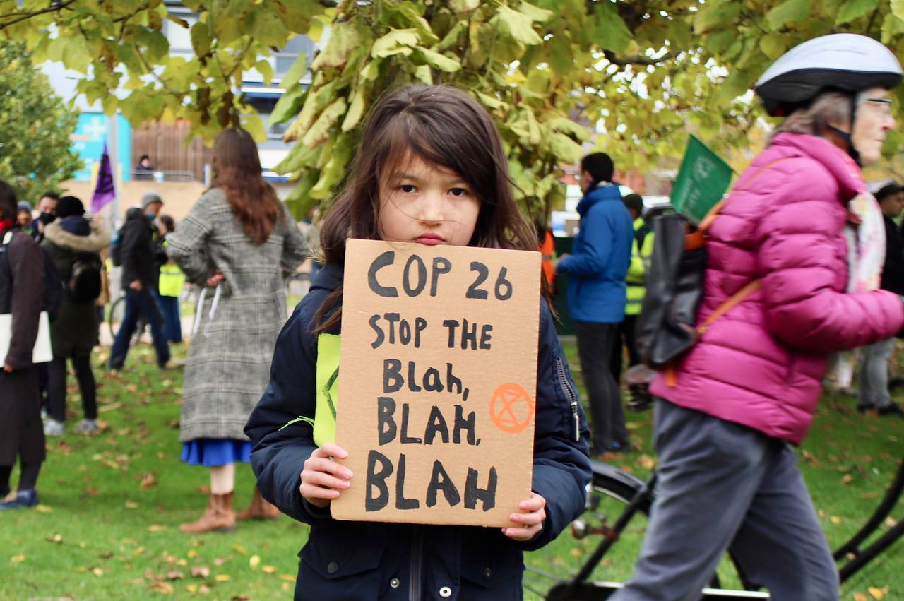 A child holds a sign: Cop 26 stop the blah blah blah