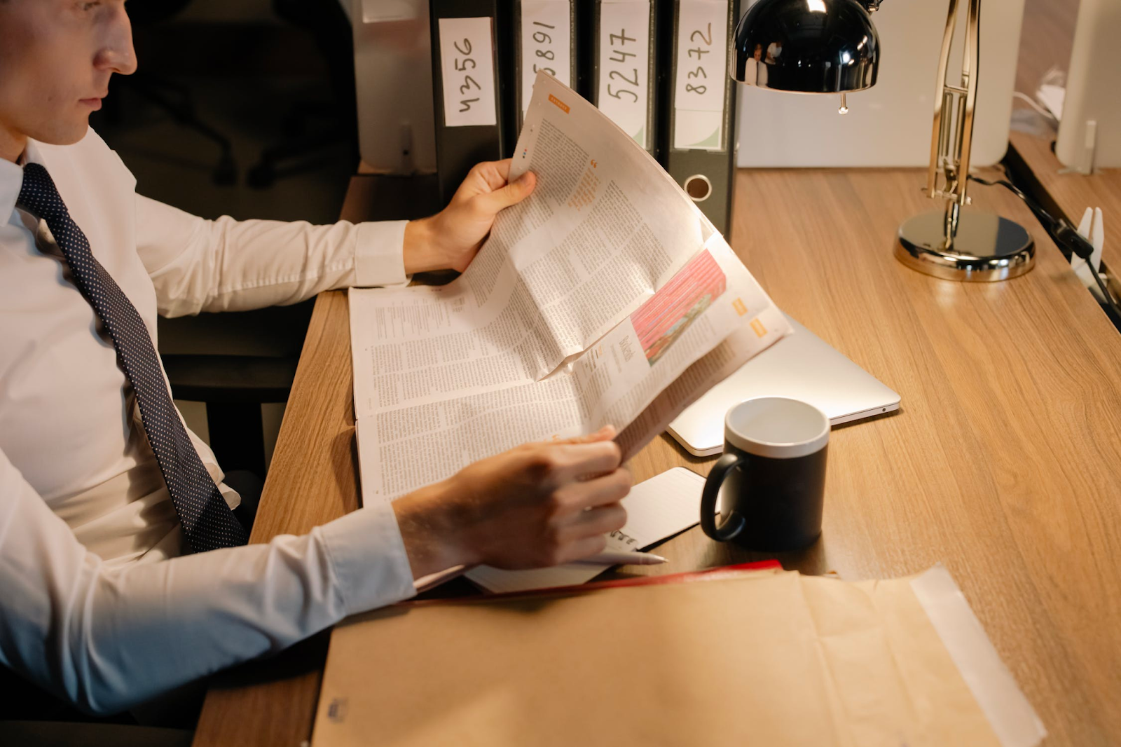 man in shirt and tie reading business publication newspaper with coffee mug at his desk considering how to get local business