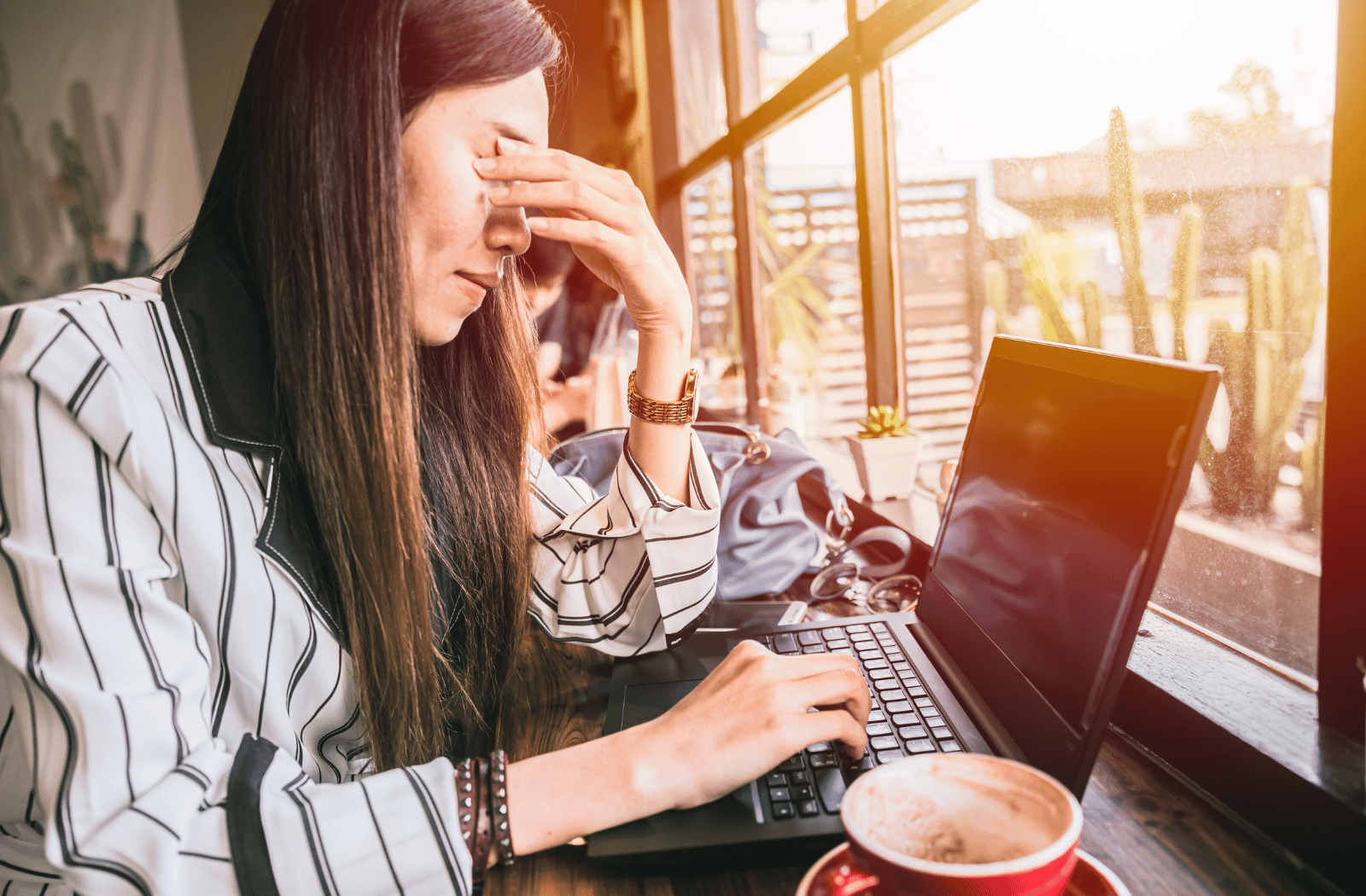 A woman sitting in a coffee shop rubbing her eyes due to looking at a computer screen for too long.