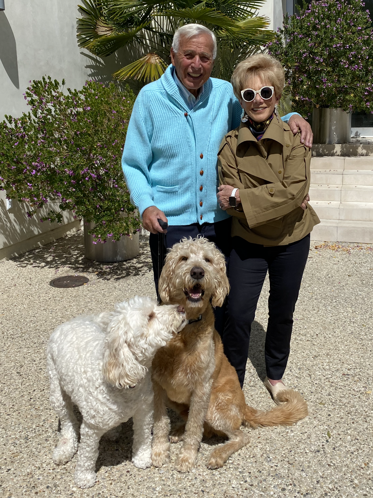 Demetrios and his wife smile for a photo with a white and golden pair of Labradoodles.