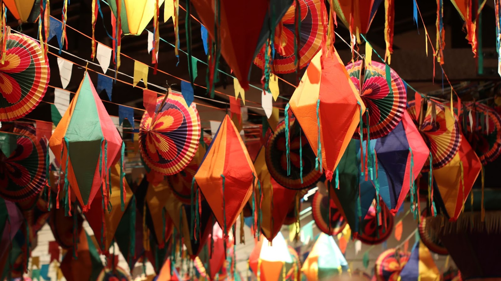 Balões e bandeirolas coloridas de papel, presas em cordões no teto, como parte da decoração de uma festa de São João.