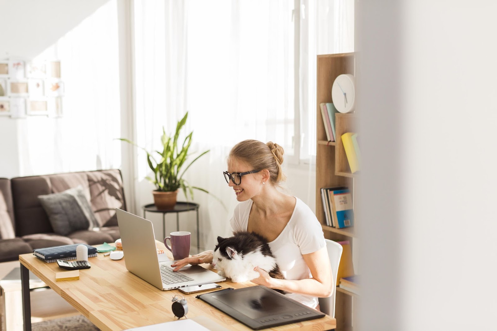 Uma mulher sentada com trabalhando em casa tendo o beneficio de poder ter seu pet em seu colo enquanto trabalha.