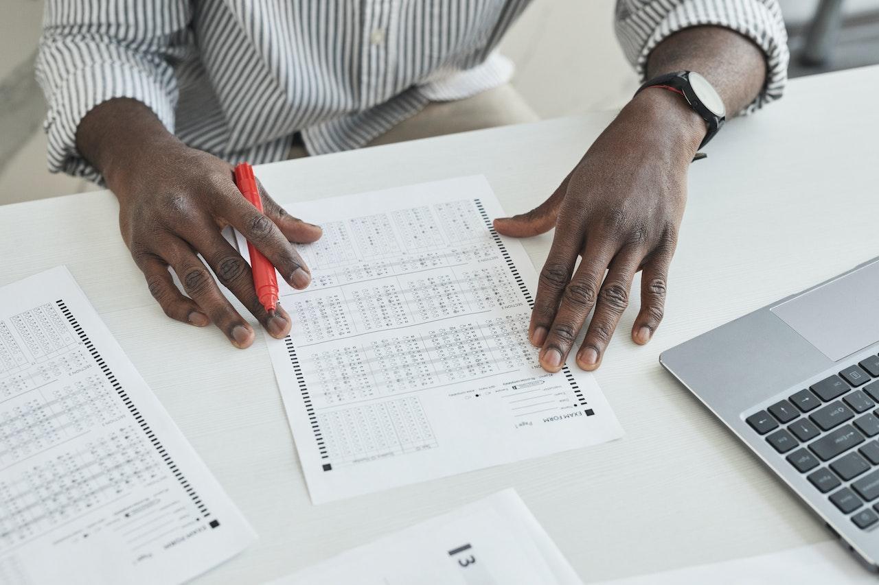 A teacher is looking onto a sheet of multiple choice questions and holding a red marking pen in his hand.