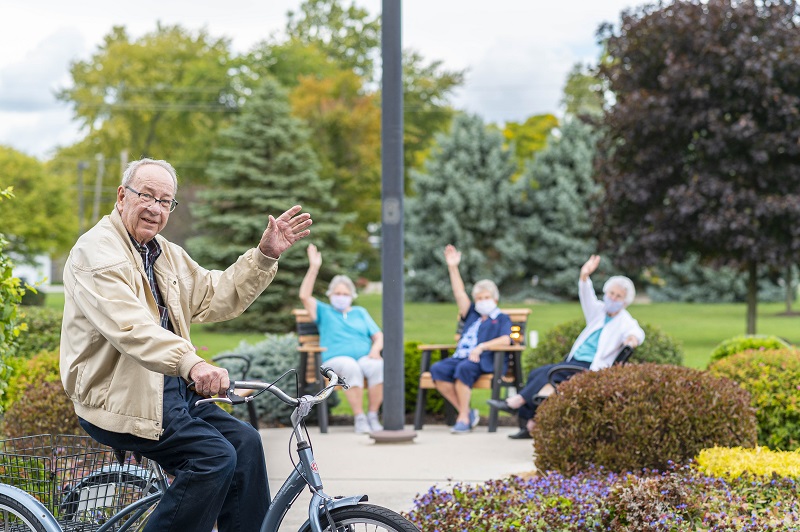 Otterbein resident rides bike on campus while neighbors wave in background