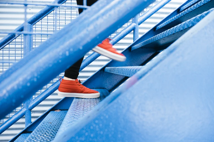 someone with orange shoes walking up blue steps. Denotes the steps needed to get a regular sleep schedule.