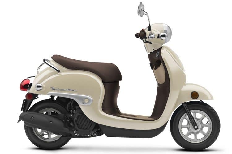 Tan and brown 2023 Honda Metropolitan scooter displaying its right side profile in a dealership showroom.