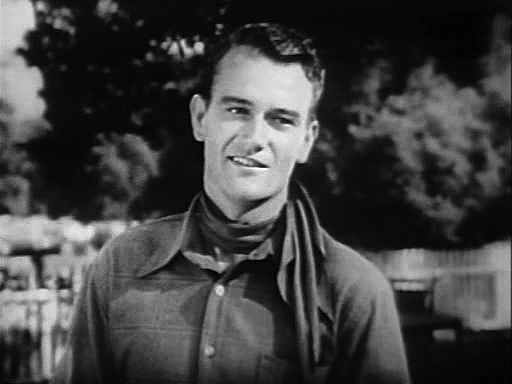 A black-and-white still frame of John Wayne as Singin’ Sandy Riders of Destiny