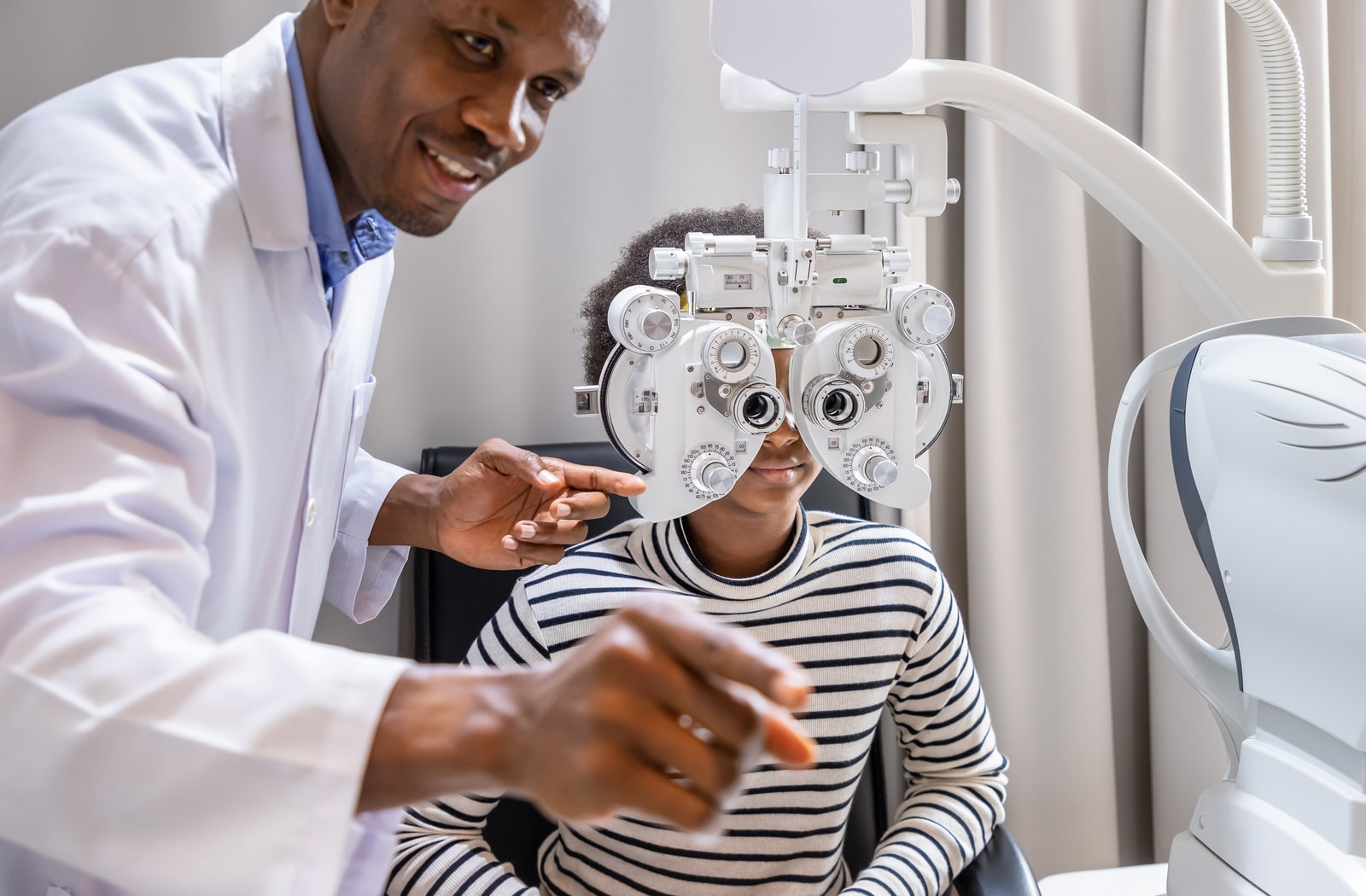 A male optometrist checking a young patient's eyes with a phoropter