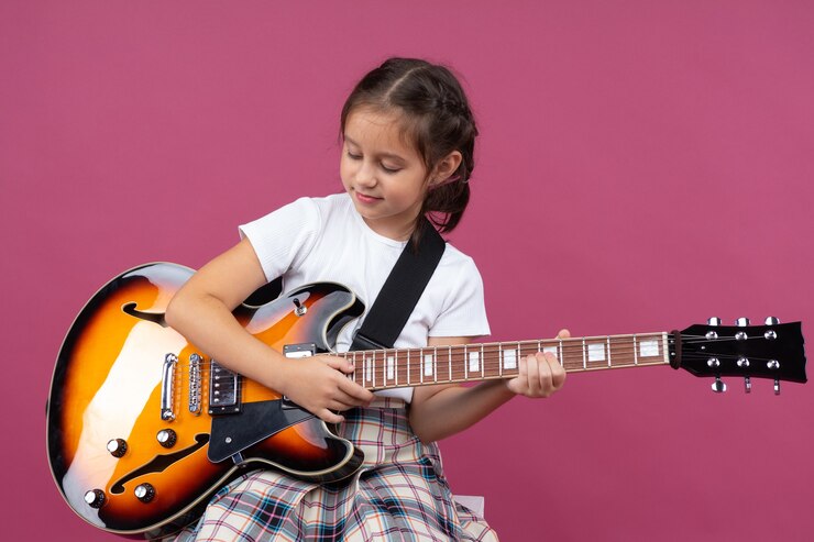 Menina de aparência satisfeita segura uma guitarra com a clássica pintura sunburst: a escolha da guitarra elétrica infantil depende do interesse da criança.