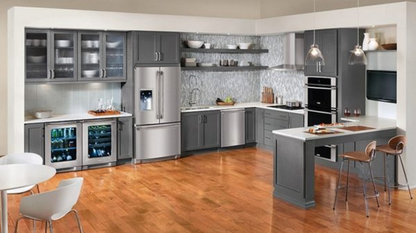 Things To Consider while cleaning kitchen cabinets. Gray kitchen cabinets and stainless steel appliances. white table and chairs. floating shelves and white and gray backsplash. 