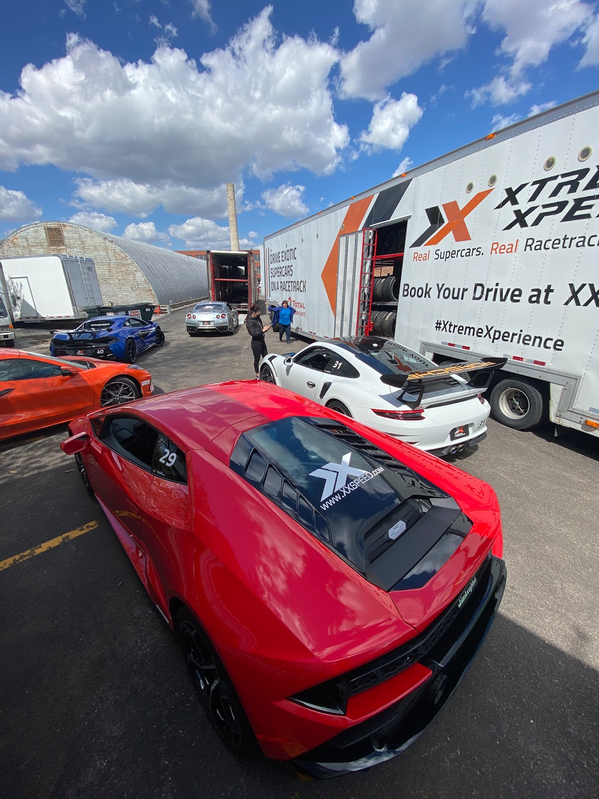Four supercars are parked outside the Xtreme Xperience garage waiting to be loaded onto a branded semi truck.