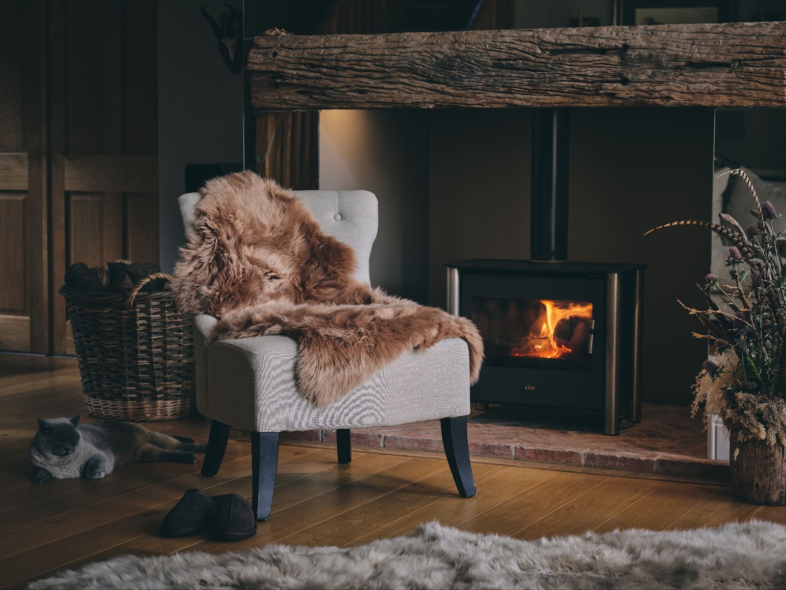 A cosy man cave, focused on a chair with a honey coloured sheepskin rug on it, wood stove burning in the background