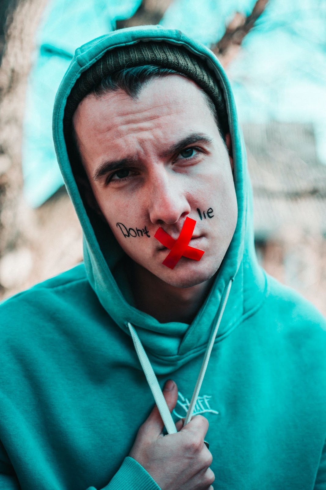 A picture of a man's face with red tap over his mouth in an X with the words don't lie written on his face, introducing the lyric "we all lie"