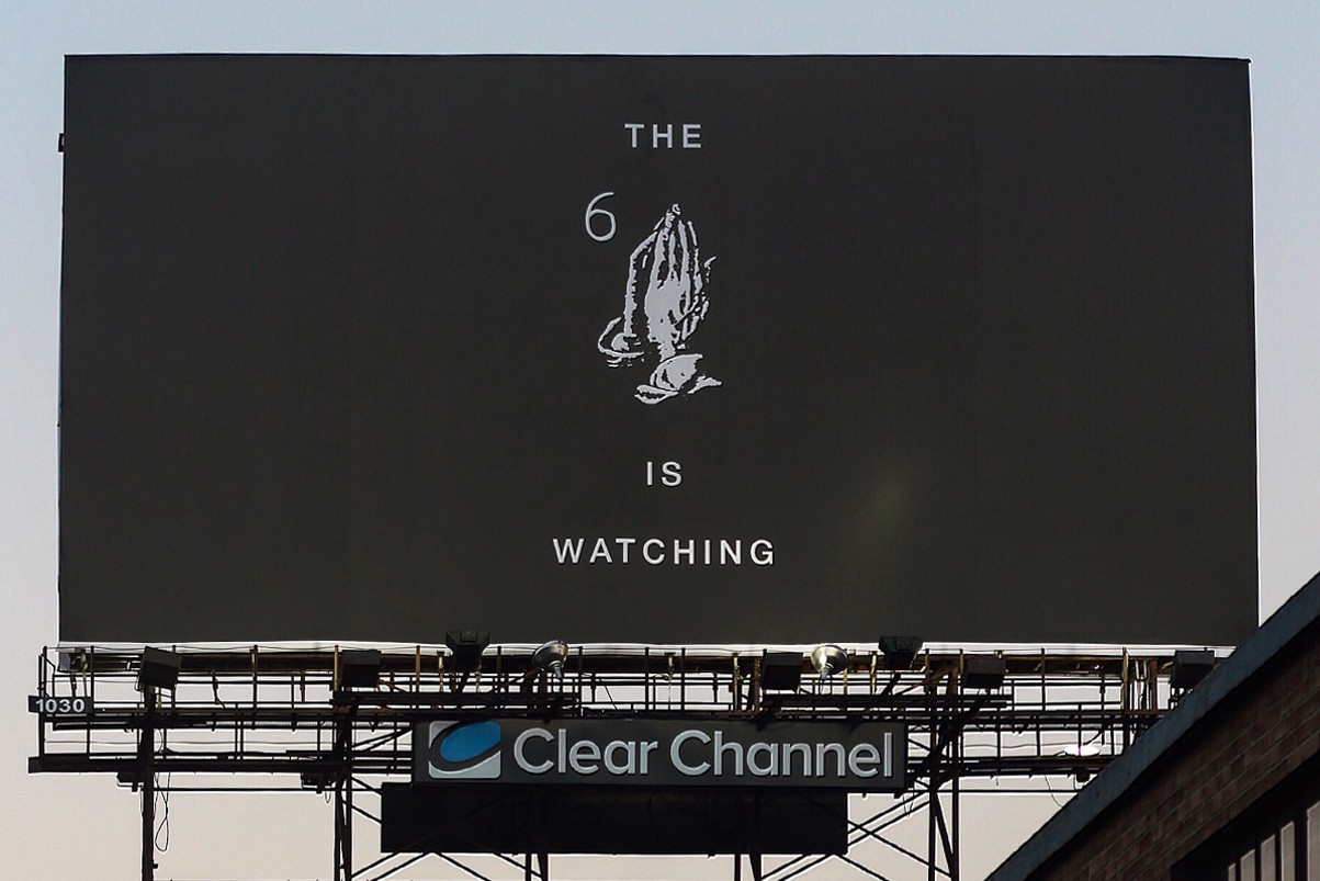 A black billboard on a highway with an image of praying hands and the text 'The 6 is watching'.