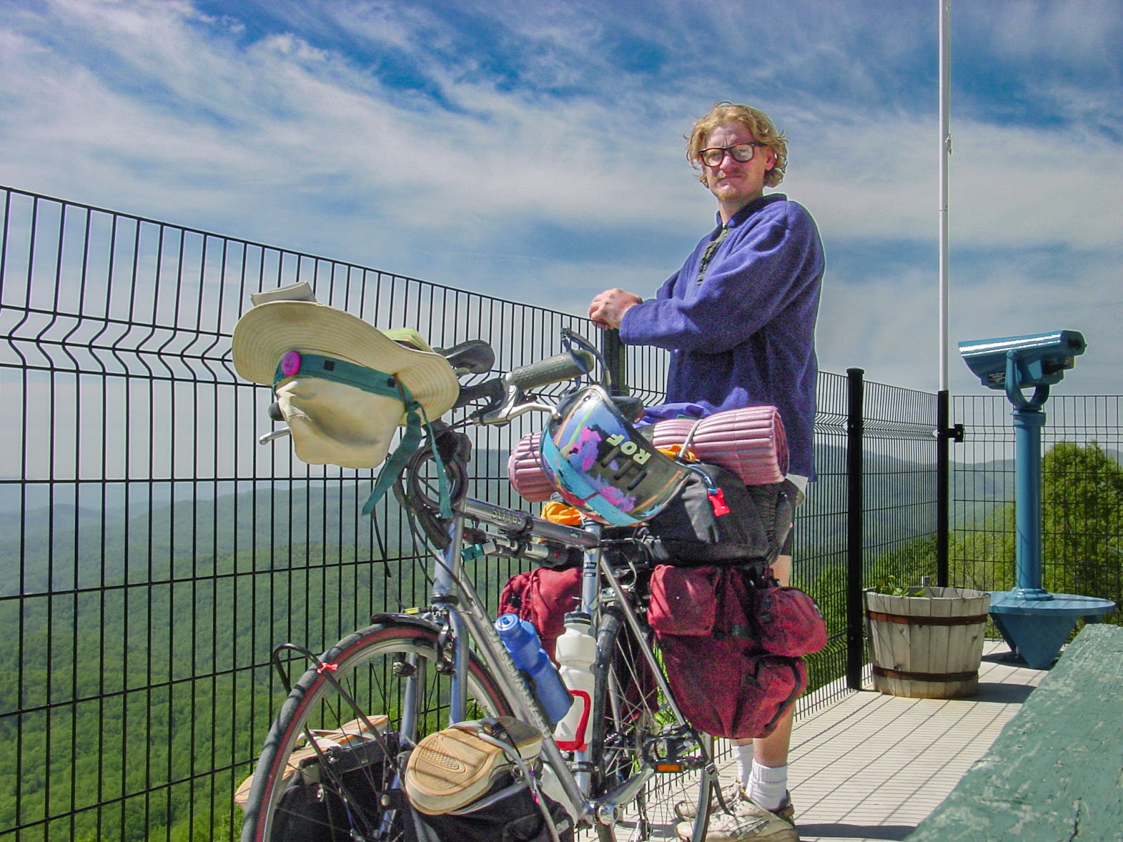 Bike loaded with camping equipment and cyclist lean on a wire fence overlook. 