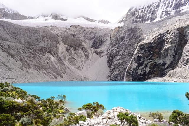 Crystal clear blue water surrounded by grey-ish, snow covered mountains in the Huascaran National Park in Peru.