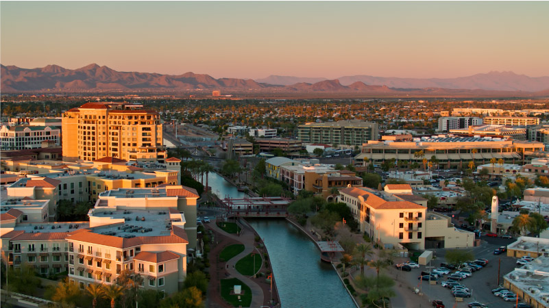 Aerial view of Downtown Scottsdale, Arizona, with the canal running through the city and the mountains in the distance.