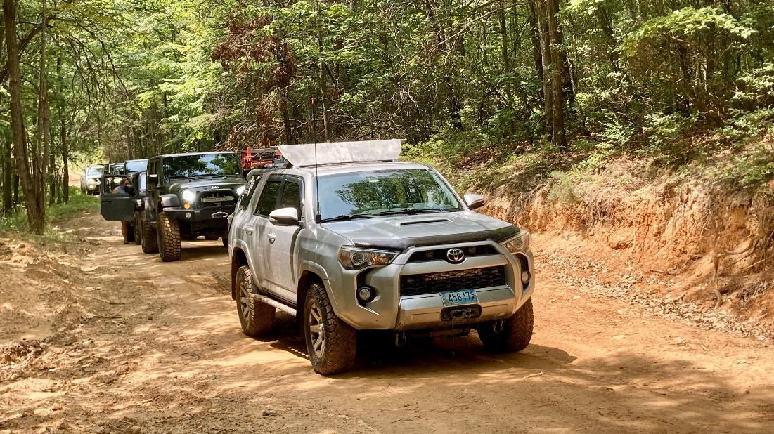 A group of cars driving on a dirt road

Description automatically generated