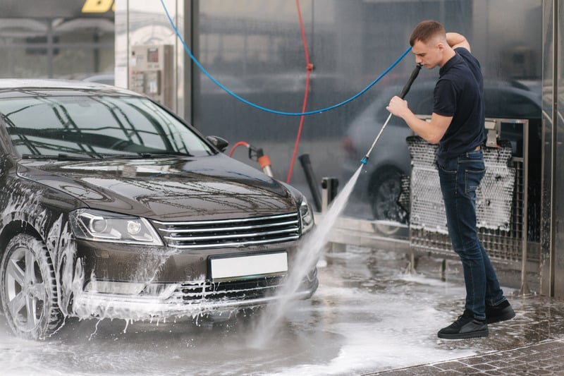 Car detailer pressure washing a vehicle