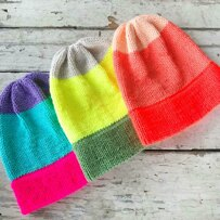three colorful knit hats lying flat on white wooden background