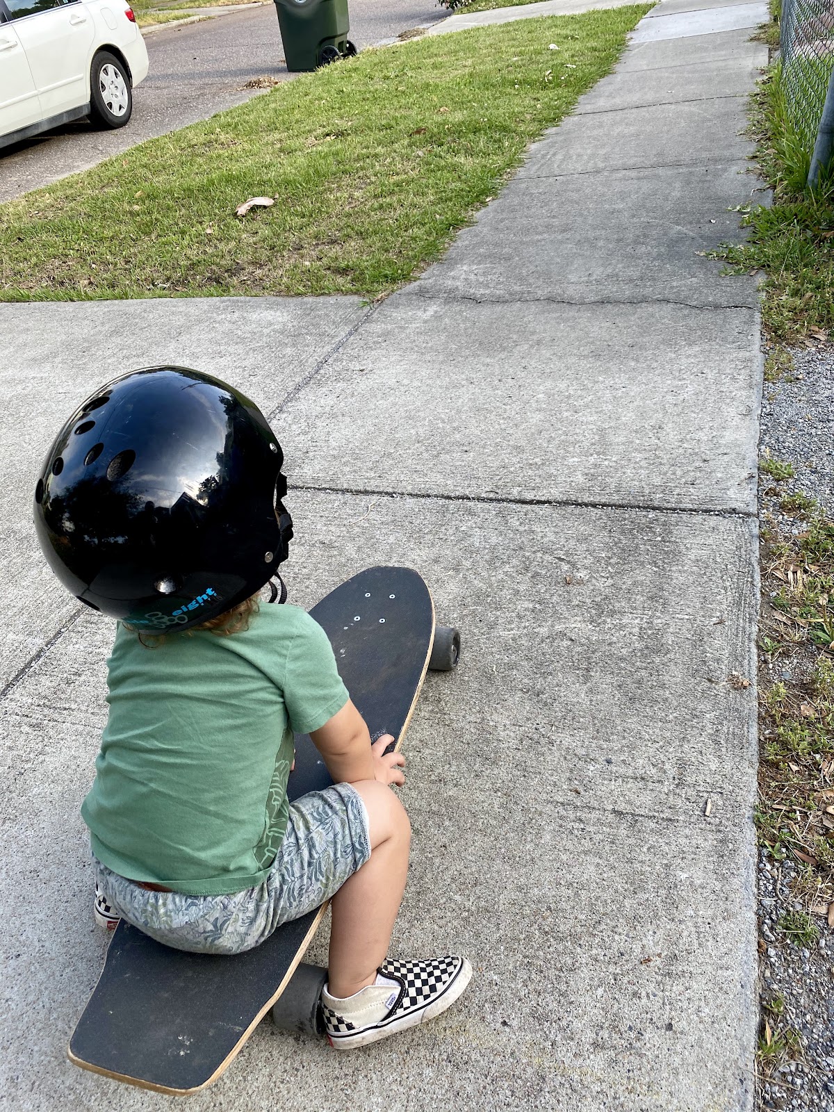 Jimmy sits on a skateboard and prepares to roll down a long sidewalk.