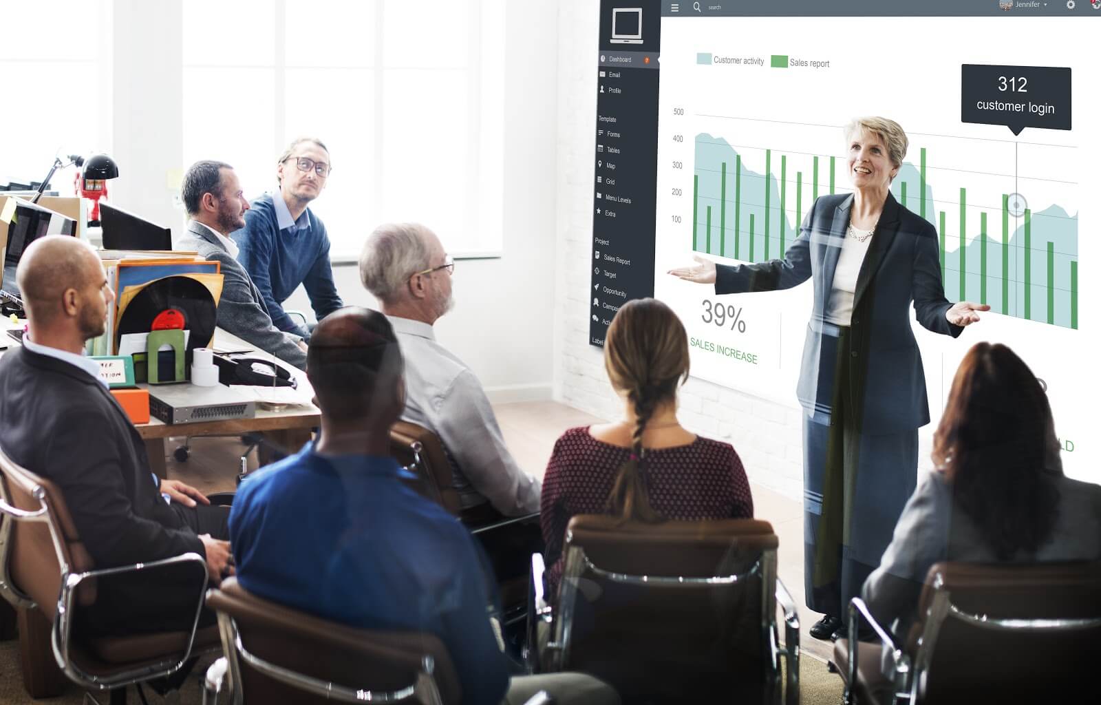 Older professional woman presenting data to room of colleagues