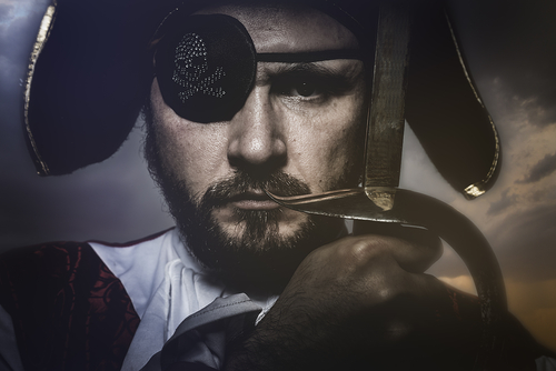 Portrait of a pirate holding a sword and sporting an eyepatch. 