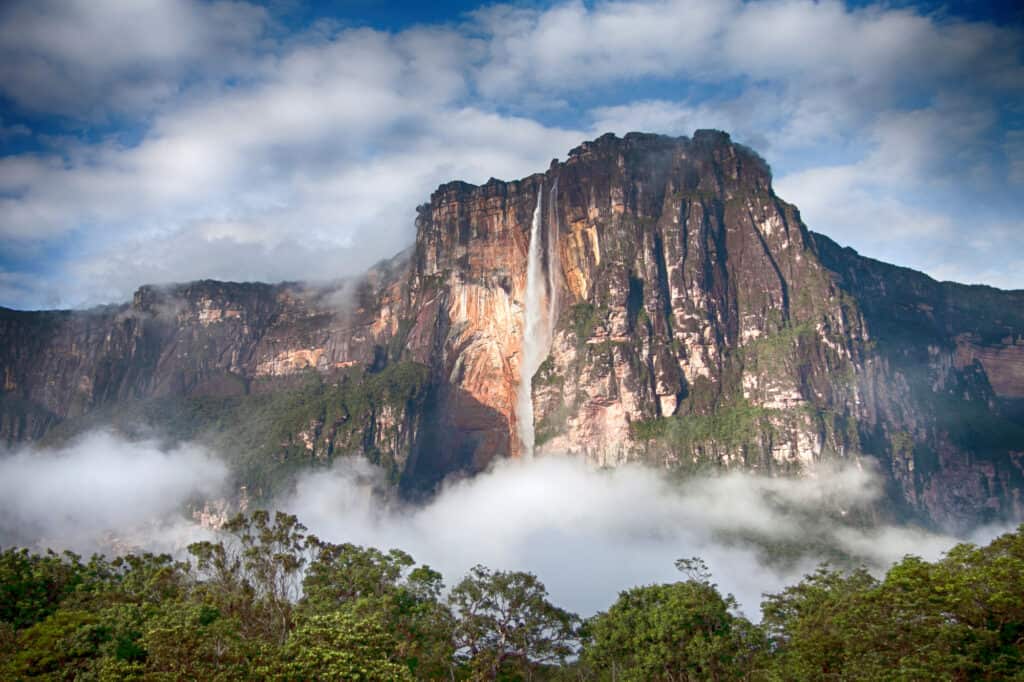 Water cascading down a very high and rocky mountainous range with clouds surrounding the base of the falls known as Angel Falls in Canaima Park in Venezuela