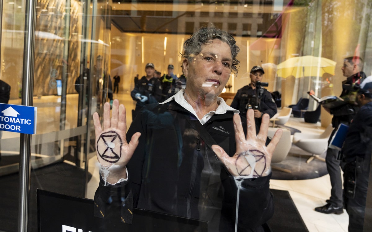 A rebel glues her XR logoed palms to a glass door of a corporate foyer