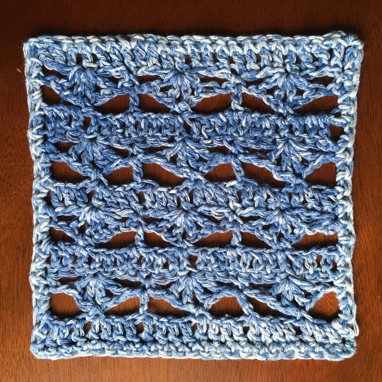 A blue and white crocheted square, featuring fan-like "windows."