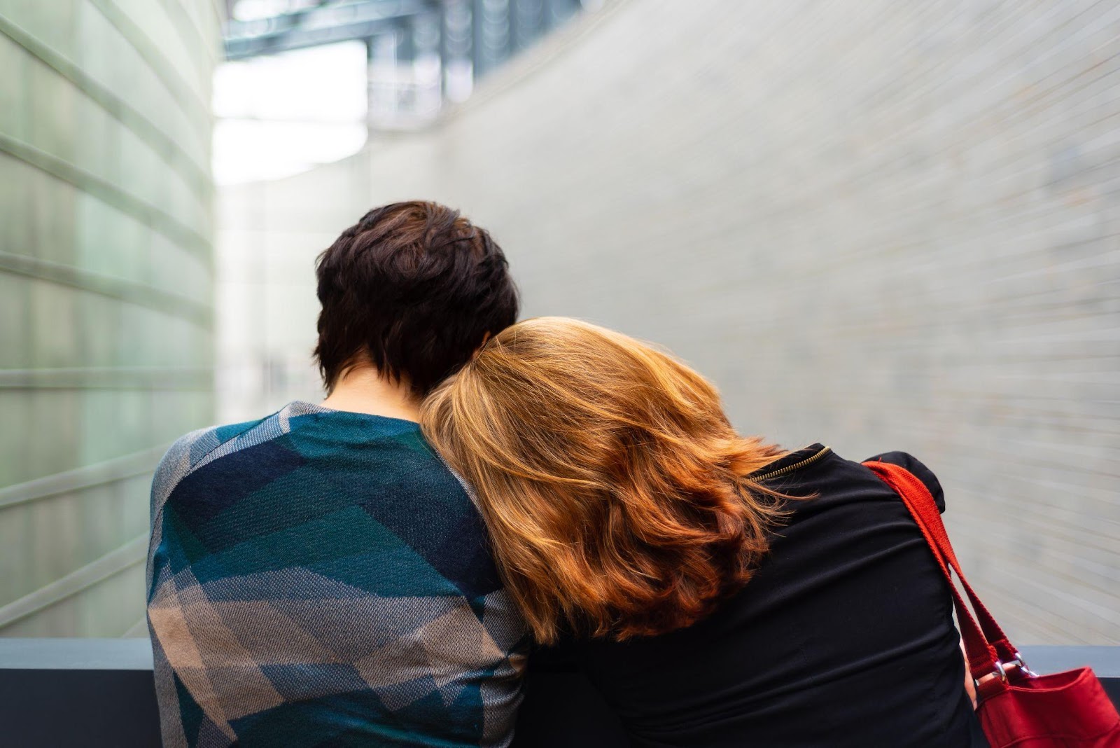 A couple standing together with the woman resting her head on the man’s shoulder.
