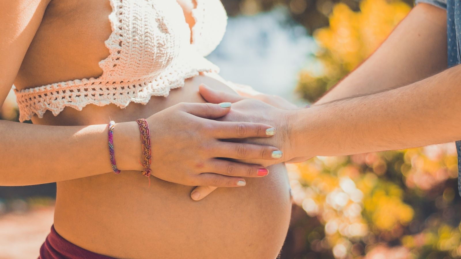 A pair of hands touch a pregnant belly.