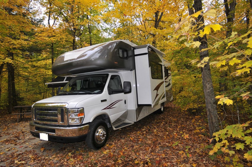 Class C RV parked under trees.