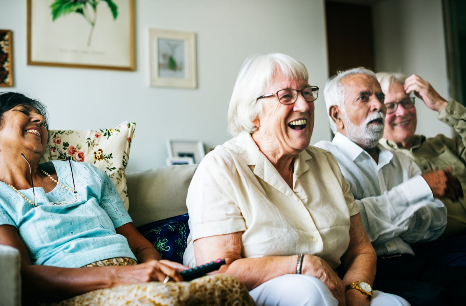 A group of four senior community residents sitting, laughing and watching TV together.