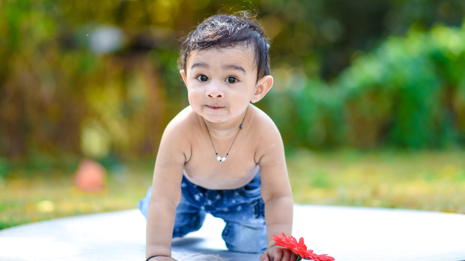 A Baby crawling on a playmat in a park. Baby-led Parenting helps babies grow at their own pace.
