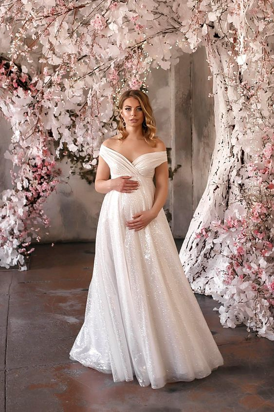 A bride wearing an empire waist maternity wedding dress with a portrait neckline