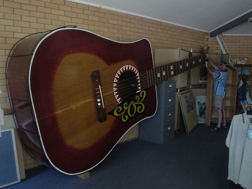 the big playable guitar is inside a room with a man playing it 
