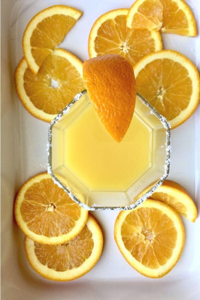 adrenal cocktail in a salt rimmed glass cup, surrounded by decorative orange slices in a white porcelain dish