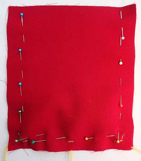 A piece of red wool fabric pinned to the previously referenced fabric with tassels before sewing in place for a bag.