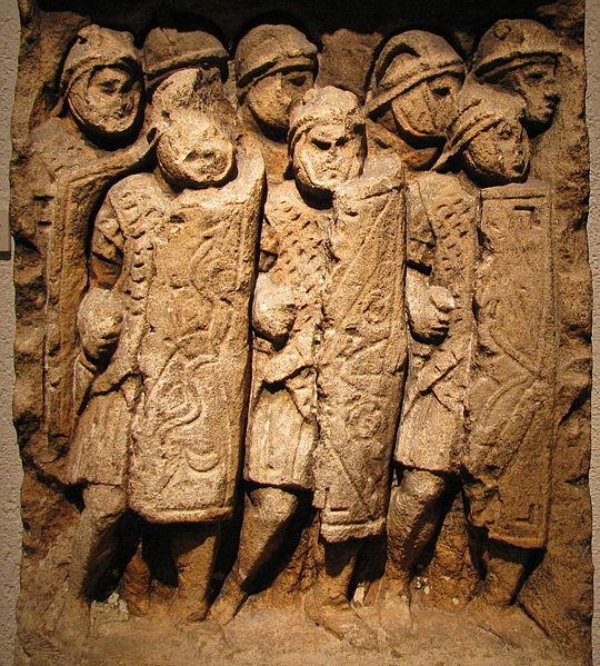 Wall carving of Roman soldiers with shields and swords.