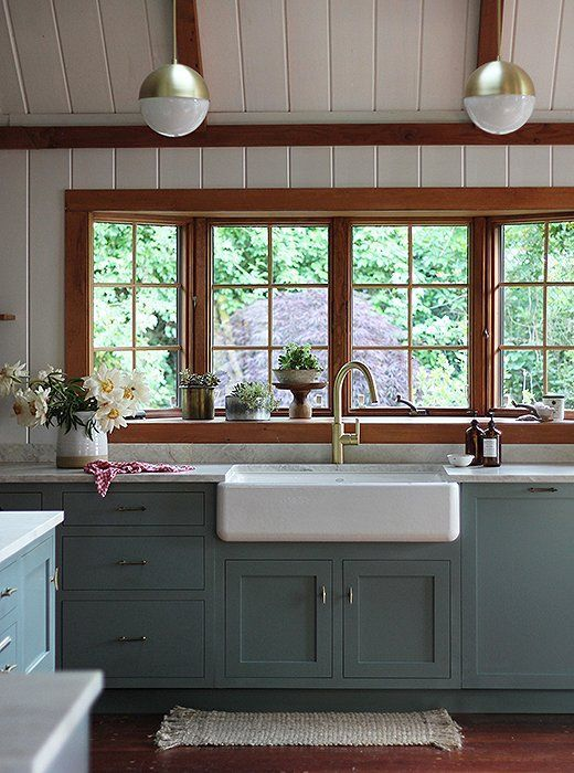 A soft and muted blue-green transforms these kitchen cabinets and makes the oak window trim and floors stand out intentionally.  How to work with honey oak to update your home.