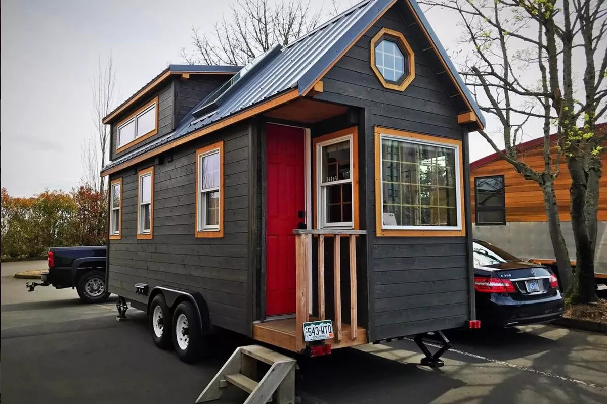 black tiny house on a trailer with wood accents, small front porch and pitched roof, tiny house kitchen ideas and photos