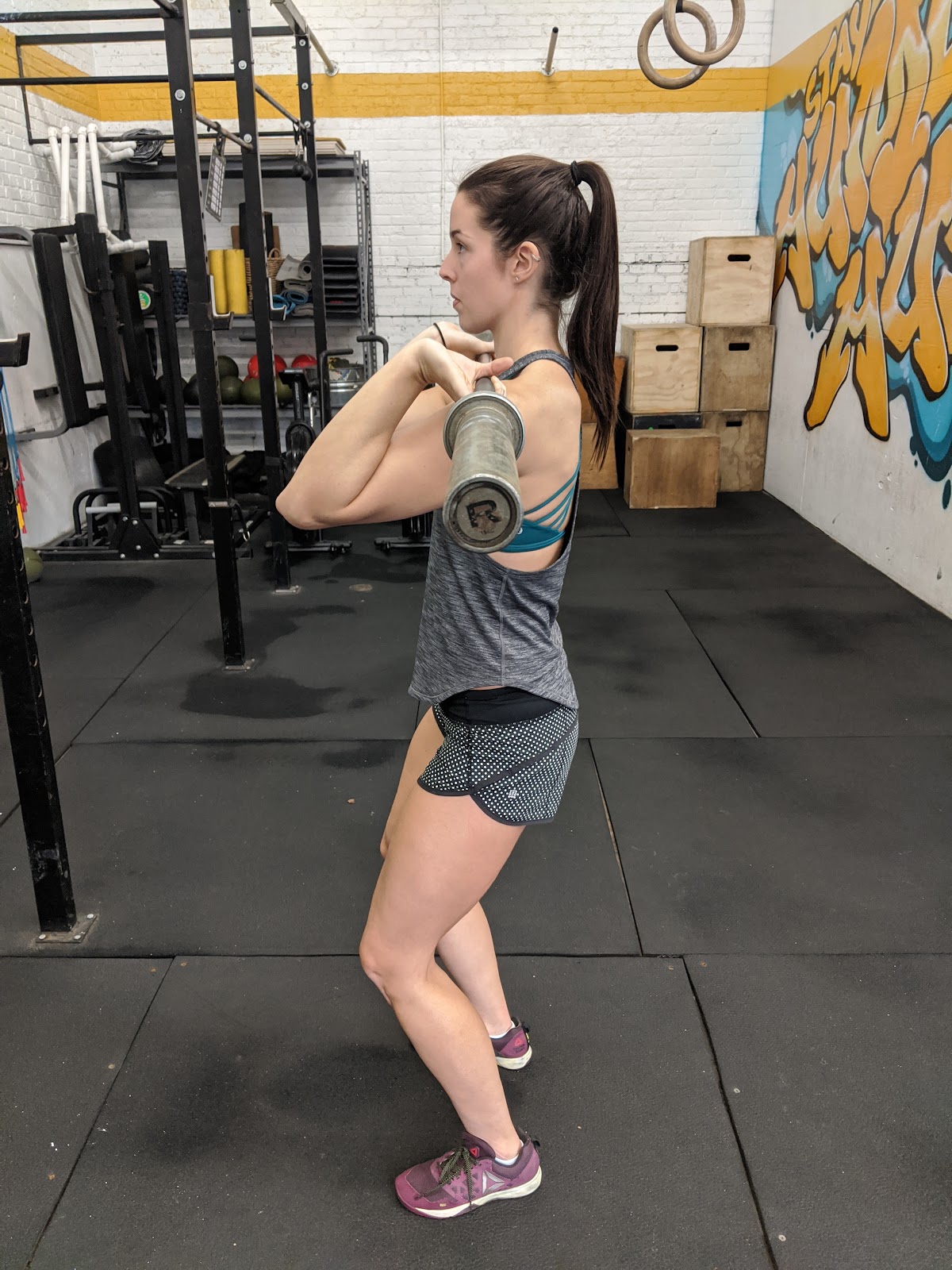 side view of woman in beginning dip position for split jerk with empty barbell on shoulders
