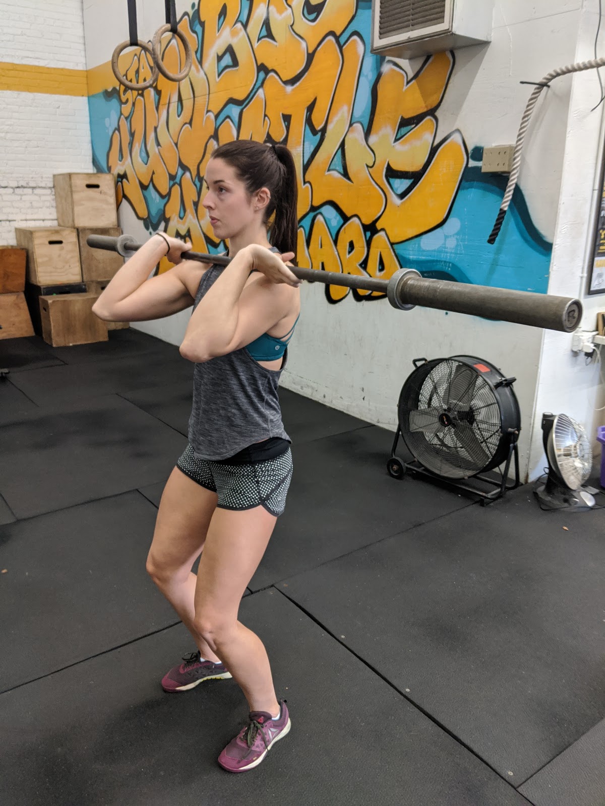 side view of woman in beginning dip position for split jerk with empty barbell on shoulders