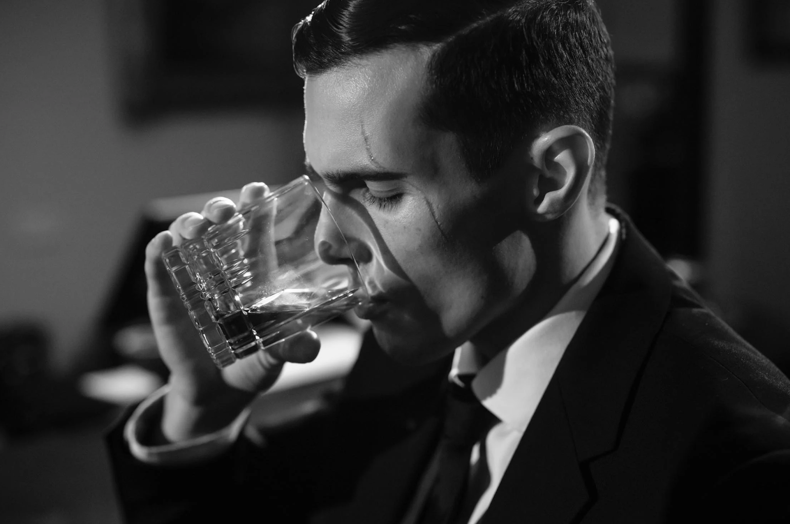 A black and white photo of a man drinking a glass of whisky.