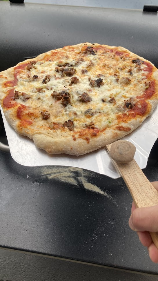 a sausage pizza on a pizza wooden handle being put on a plate
