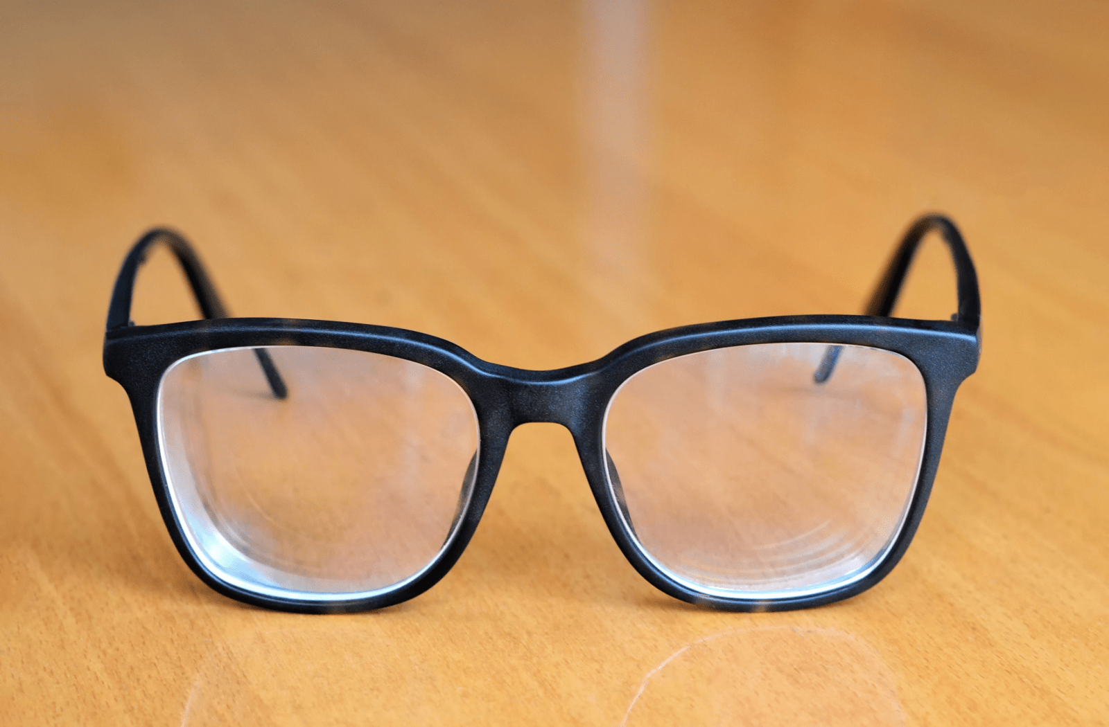 Glasses with thicker lenses, sitting on a wooden table