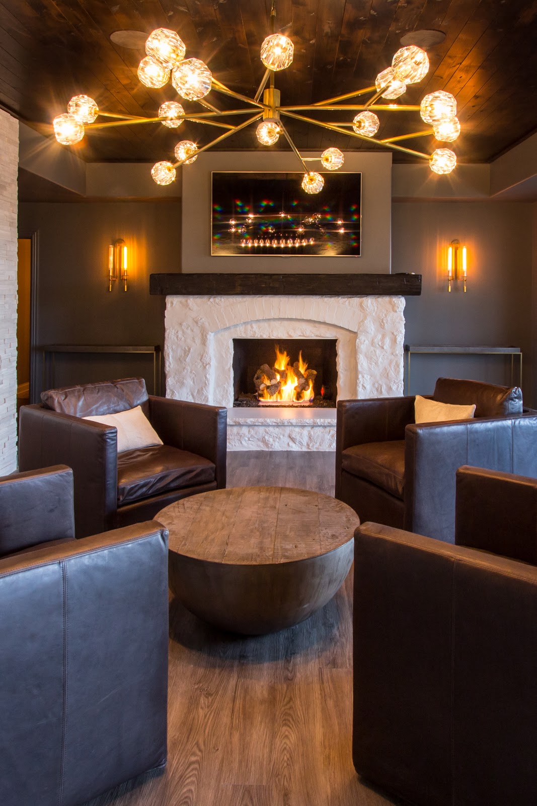 Cozy fireplace setting with leather chairs set for conversation around a weathered wood coffee table, featuring warm lighting with modern star fixture and wall sconces