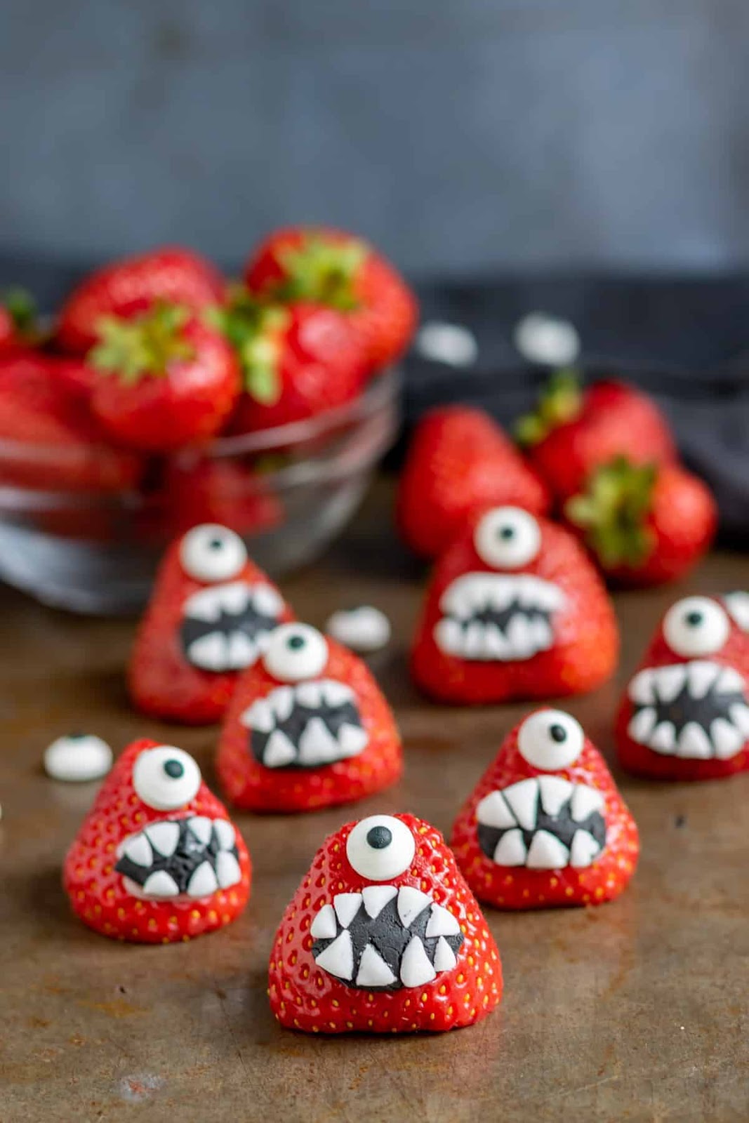 Halloween strawberry monsters on a wooden cutting board.